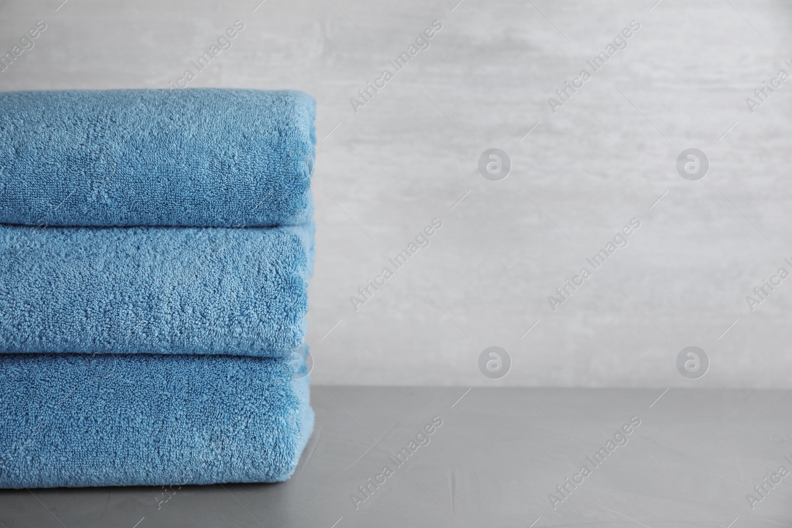 Photo of Stack of clean bath towels on grey table. Space for text