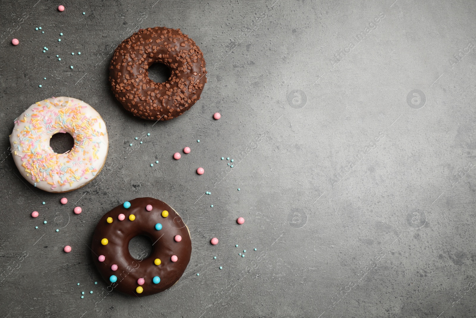 Photo of Yummy donuts with colorful sprinkles on dark table, flat lay. Space for text