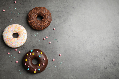 Photo of Yummy donuts with colorful sprinkles on dark table, flat lay. Space for text