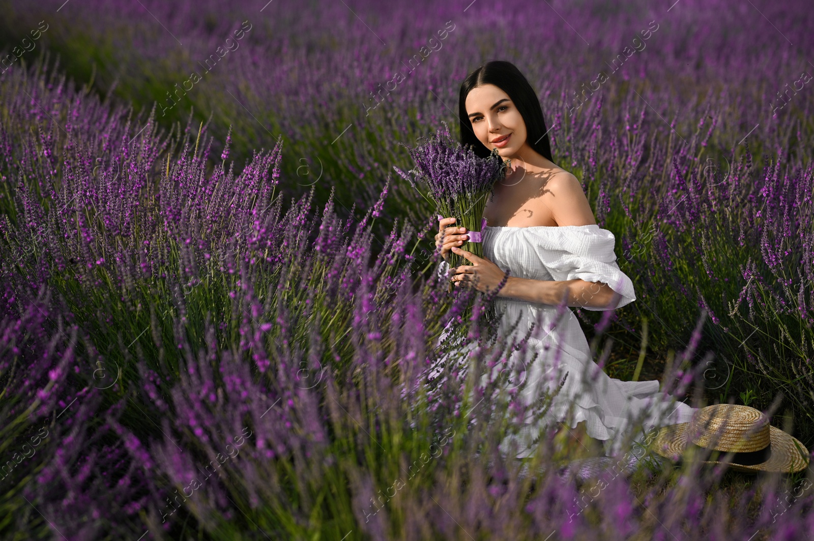 Photo of Beautiful young woman with bouquet sitting in lavender field