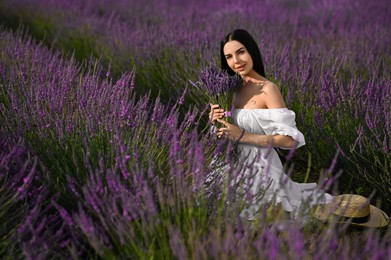 Photo of Beautiful young woman with bouquet sitting in lavender field