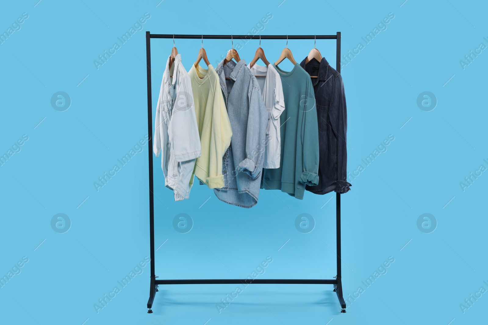 Photo of Rack with stylish clothes on wooden hangers against light blue background