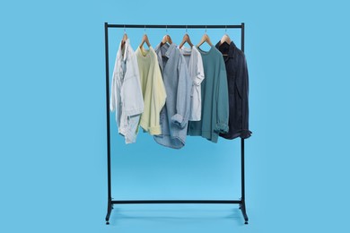 Rack with stylish clothes on wooden hangers against light blue background