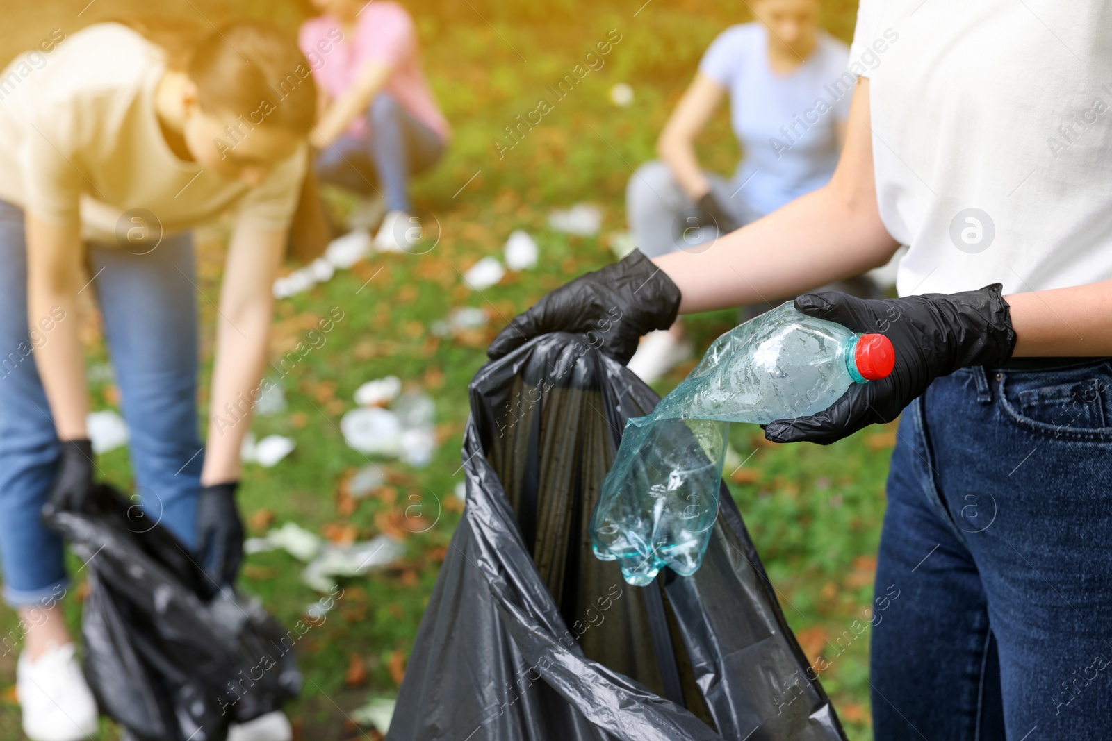 Photo of Woman with plastic bag collecting garbage in park, closeup