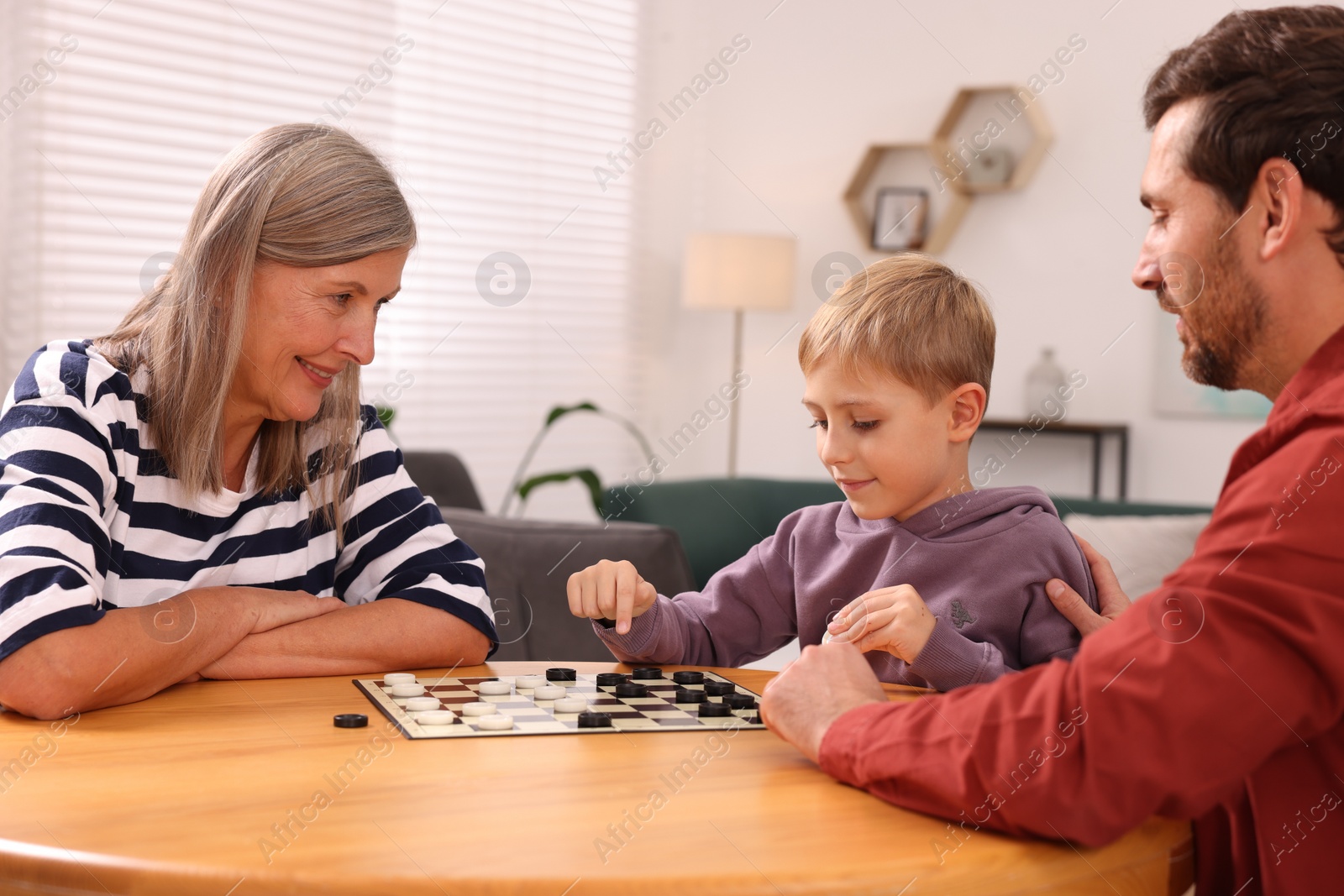 Photo of Family playing checkers at wooden table in room