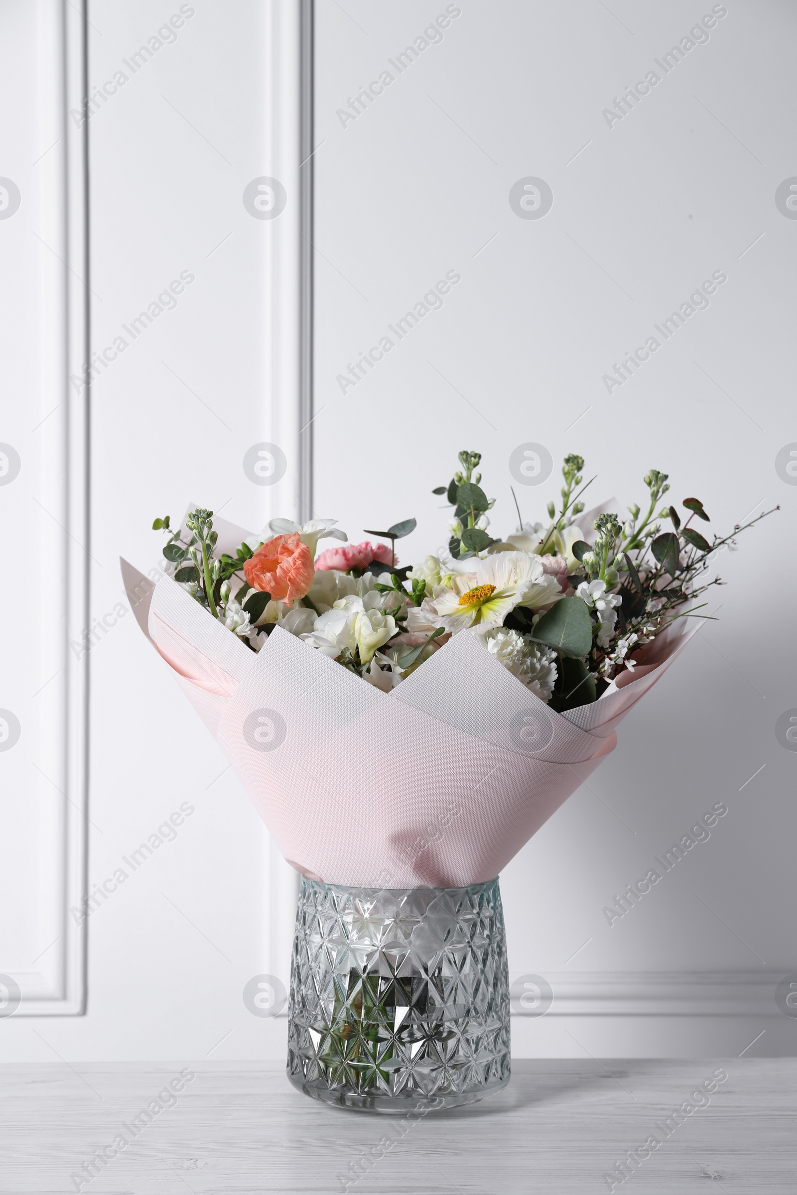 Photo of Bouquet of beautiful flowers in vase on wooden table against white wall