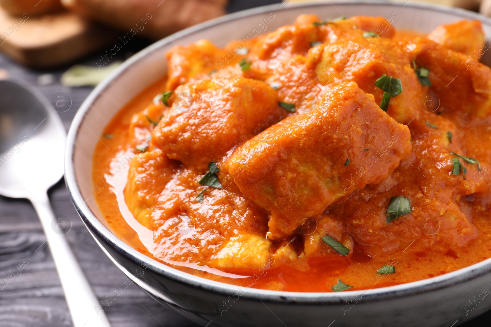 Photo of Bowl of delicious chicken curry on black wooden table, closeup