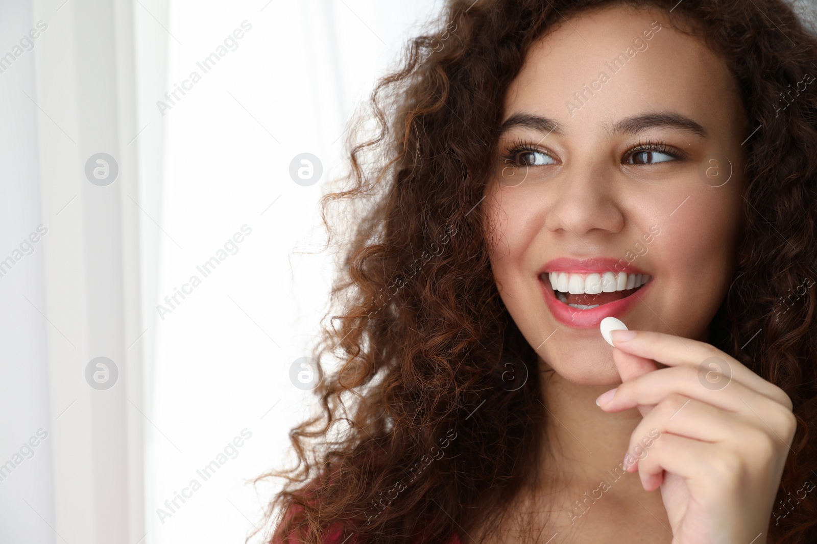 Photo of African-American woman taking vitamin pill on light background. Space for text