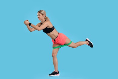 Woman exercising with elastic resistance band on light blue background