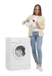 Beautiful young woman pouring detergent into cap near washing machine on white background