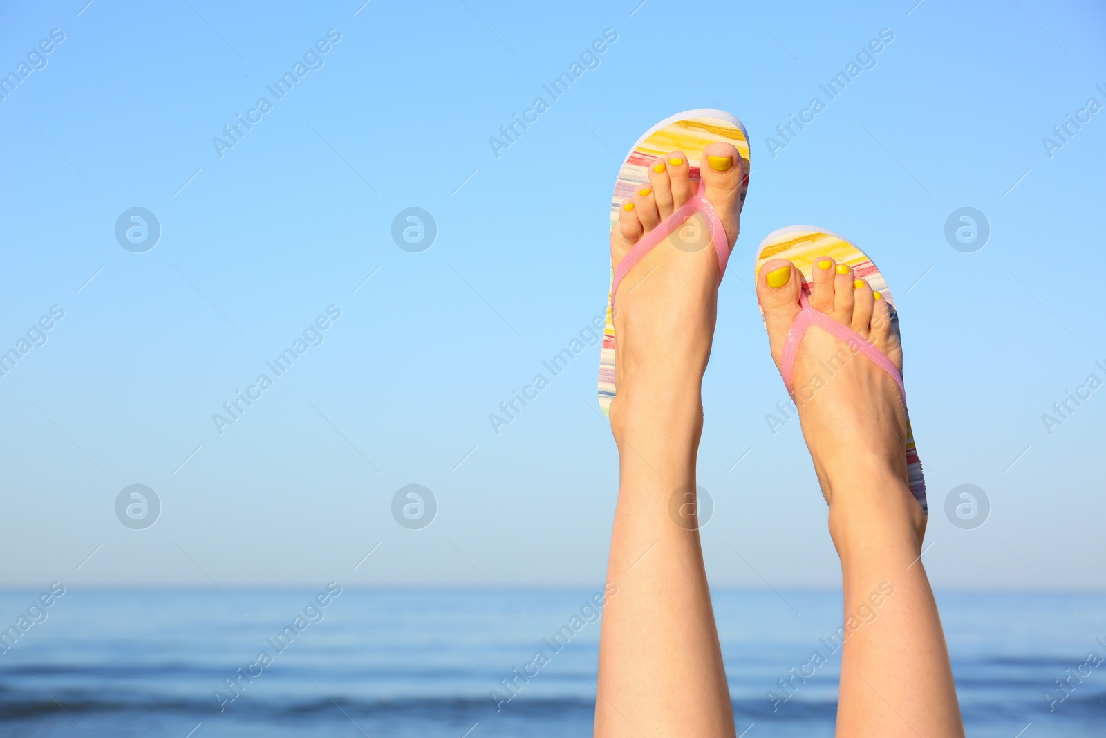 Photo of Closeup of woman wearing flip flops near sea, space for text. Beach accessories