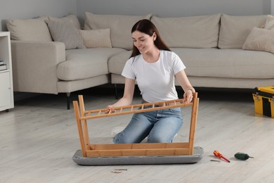 Photo of Young woman assembling shoe storage bench on floor at home