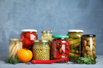 Glass jars with different pickled vegetables on table