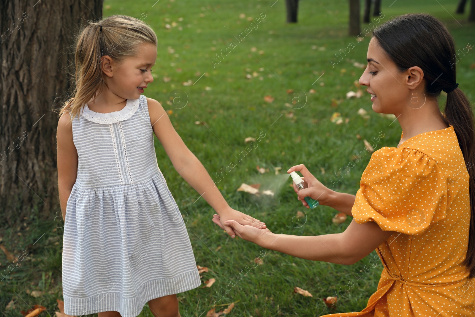 Photo of Mother applying insect repellent onto girl's hand in park