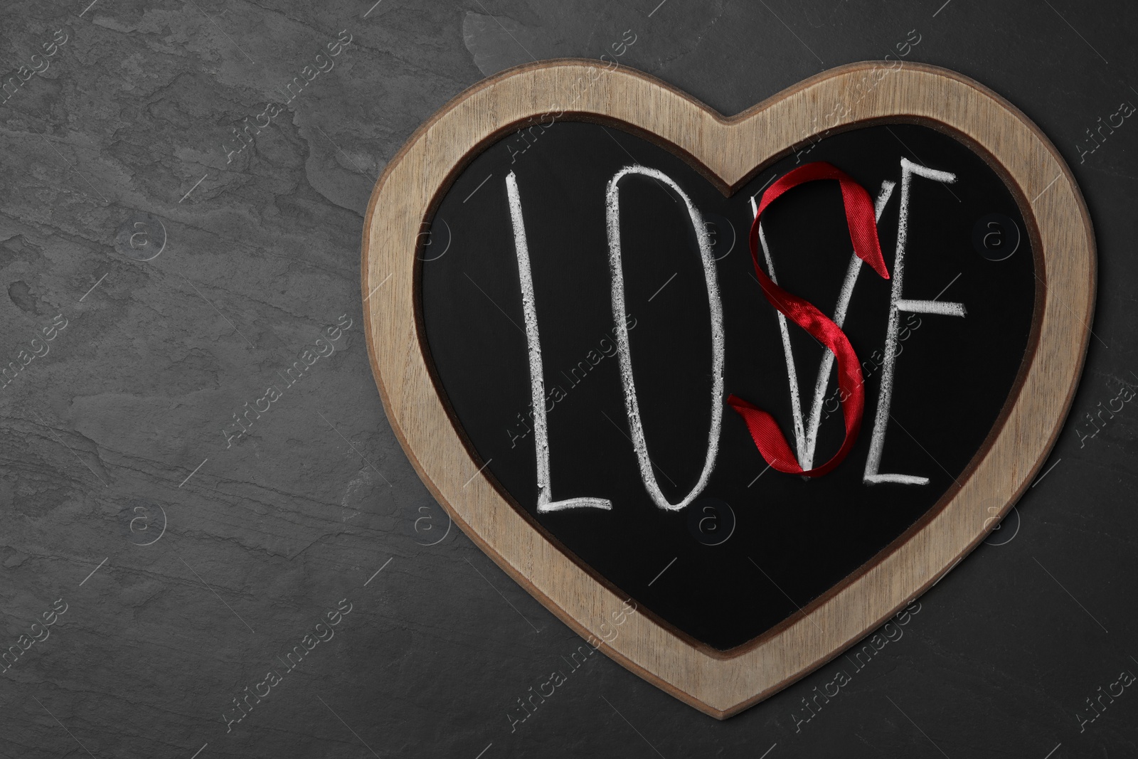 Photo of Heart shaped blackboard with word LOVE and letter S of red ribbon on dark background, top view. Composition symbolizing problems in relationship