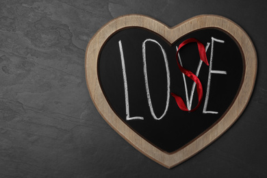 Photo of Heart shaped blackboard with word LOVE and letter S of red ribbon on dark background, top view. Composition symbolizing problems in relationship