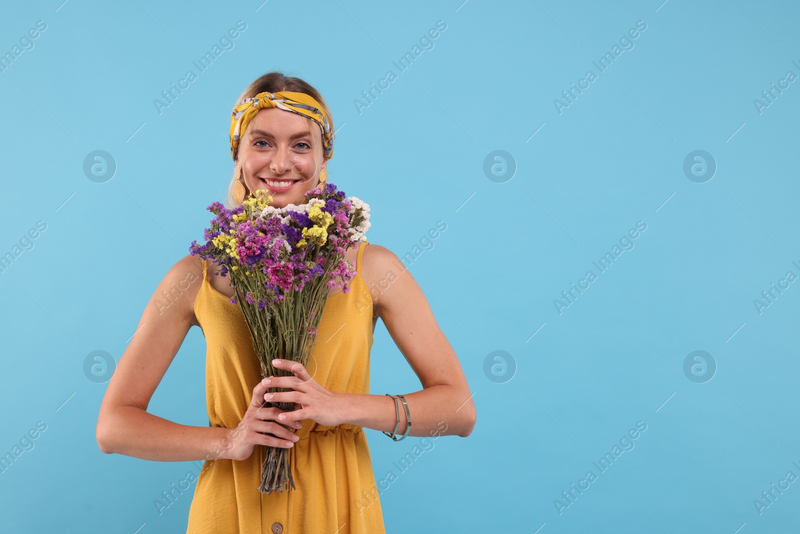 Photo of Portrait of smiling hippie woman with bouquet of flowers on light blue background. Space for text