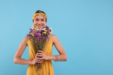 Photo of Portrait of smiling hippie woman with bouquet of flowers on light blue background. Space for text