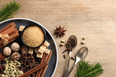 Photo of Plate with different aromatic spices, spoons and fir branches on wooden table, flat lay. Space for text