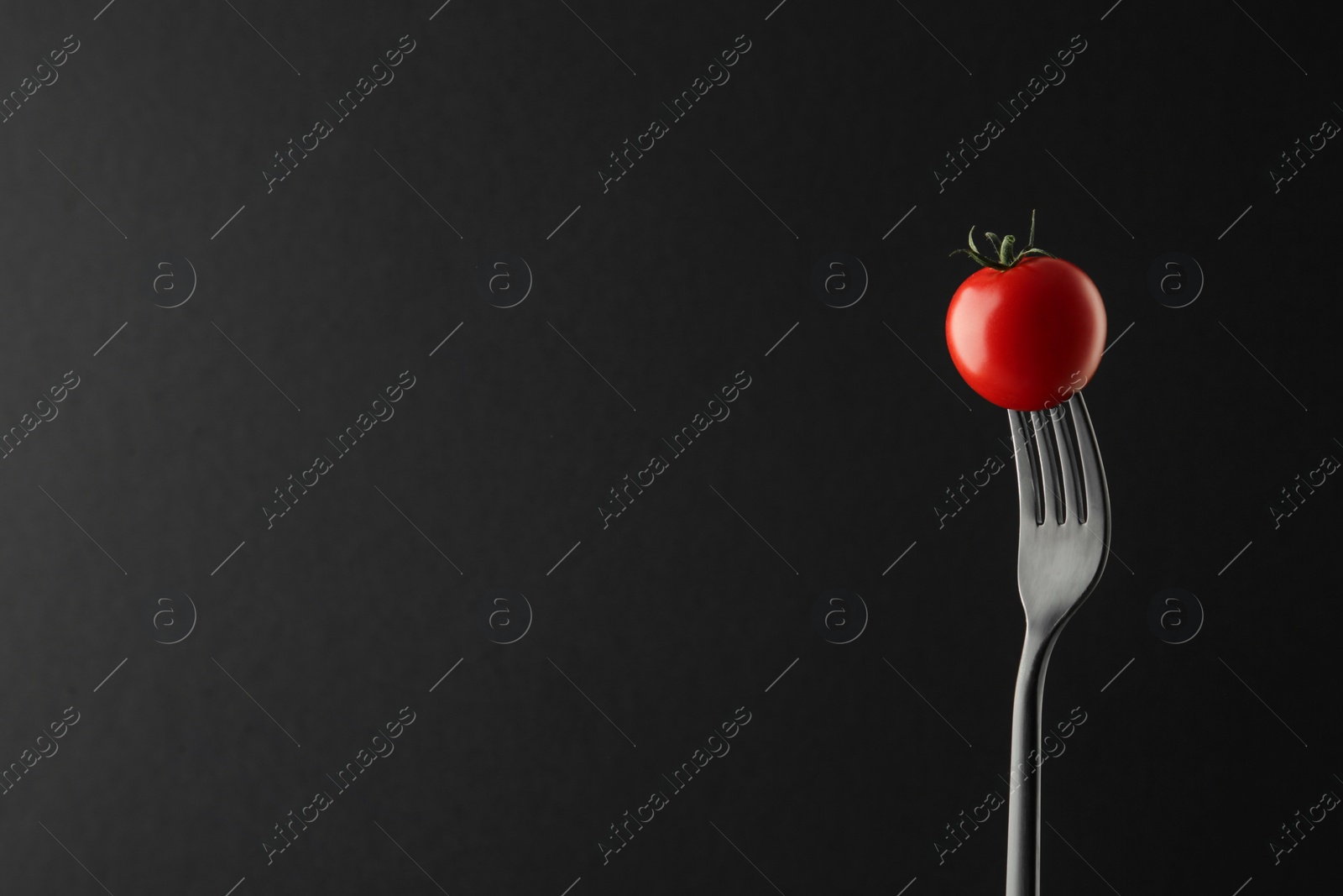 Photo of Fork with cherry tomato on black background, space for text