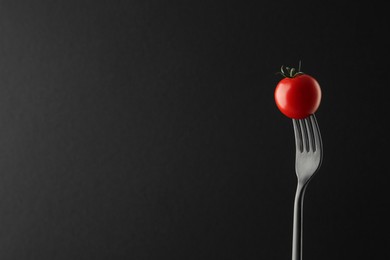 Fork with cherry tomato on black background, space for text