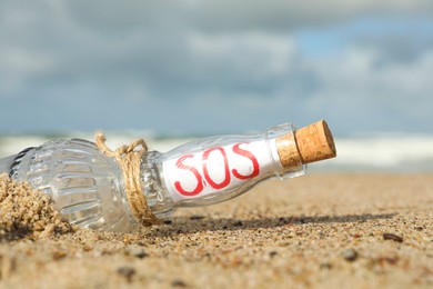 Photo of Glass bottle with SOS message in sandy beach, closeup