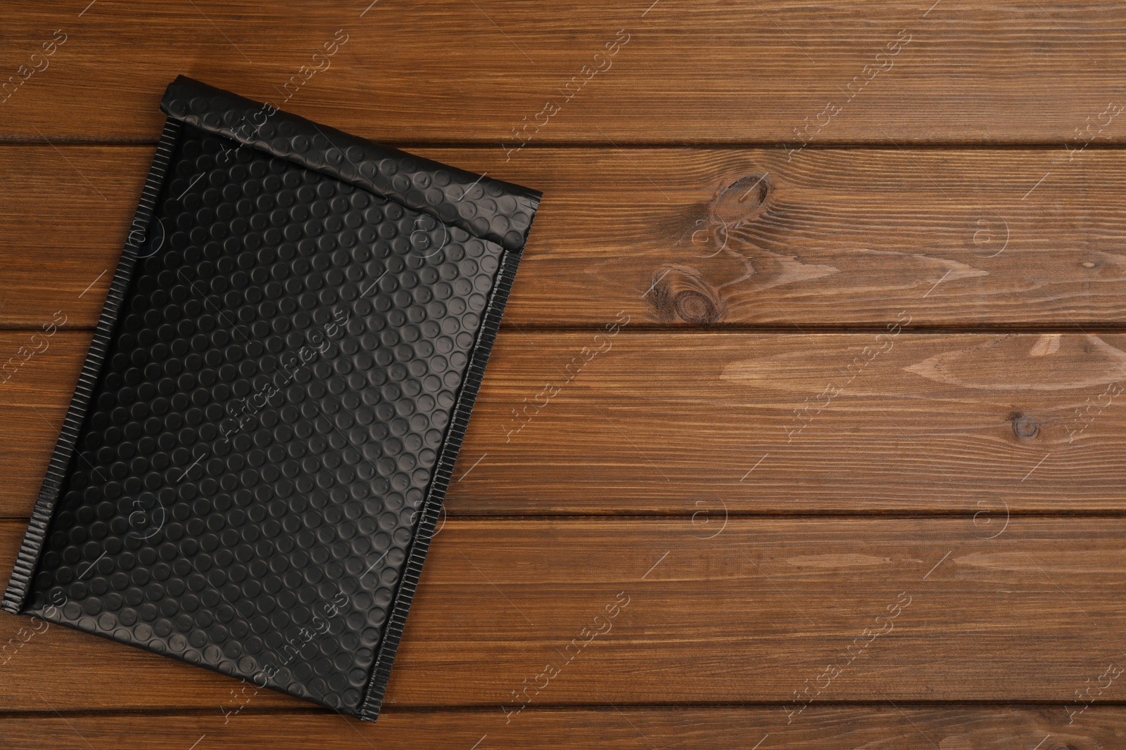 Photo of Black padded envelope with bubble wrap on wooden background, top view. Space for text