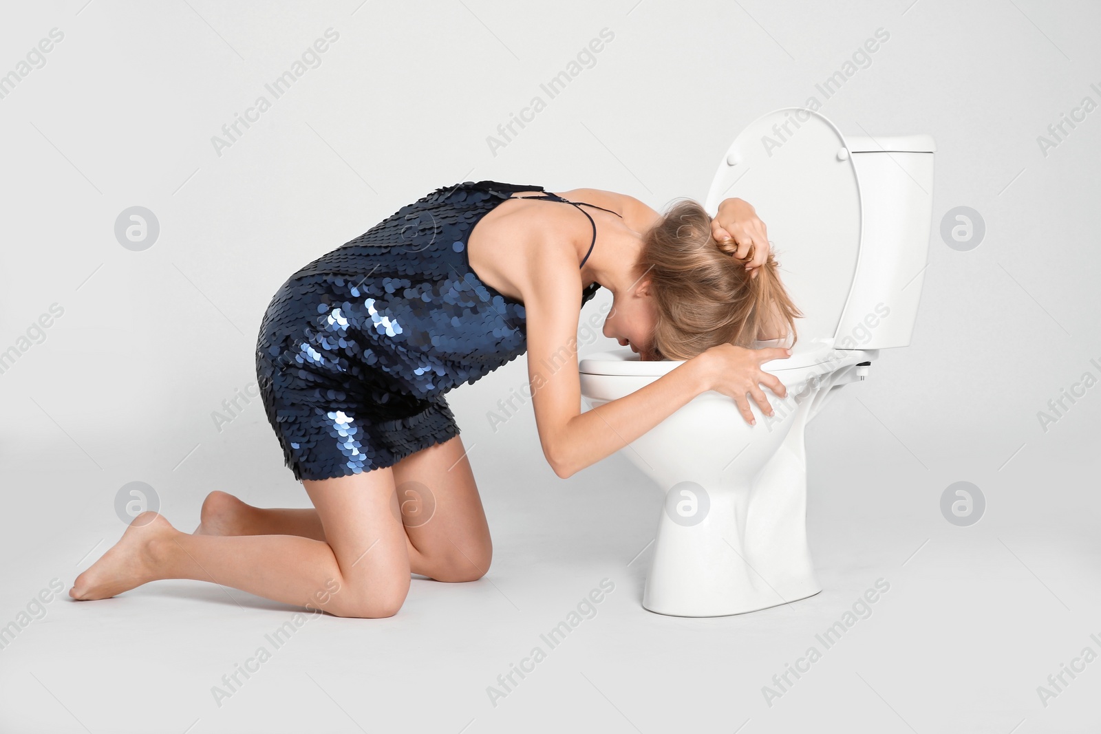 Photo of Young woman vomiting in toilet bowl on gray background