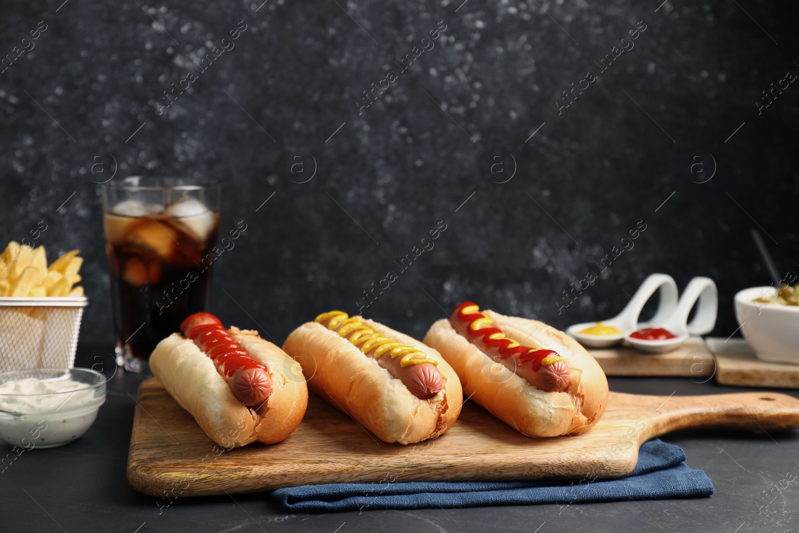 Photo of Fresh delicious hot dogs with sauces served on black table