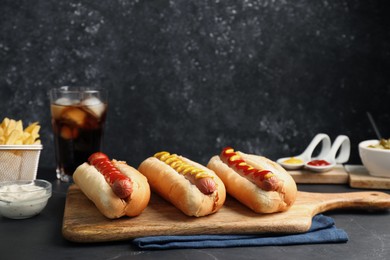 Photo of Fresh delicious hot dogs with sauces served on black table