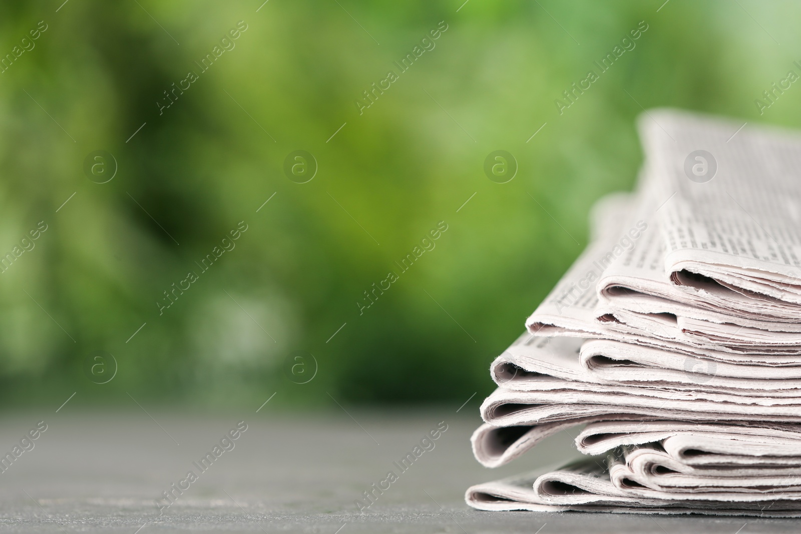 Photo of Stack of newspapers on grey table against blurred green background, space for text. Journalist's work