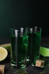 Absinthe in shot glasses, spoon and brown sugar on gray textured table. Alcoholic drink