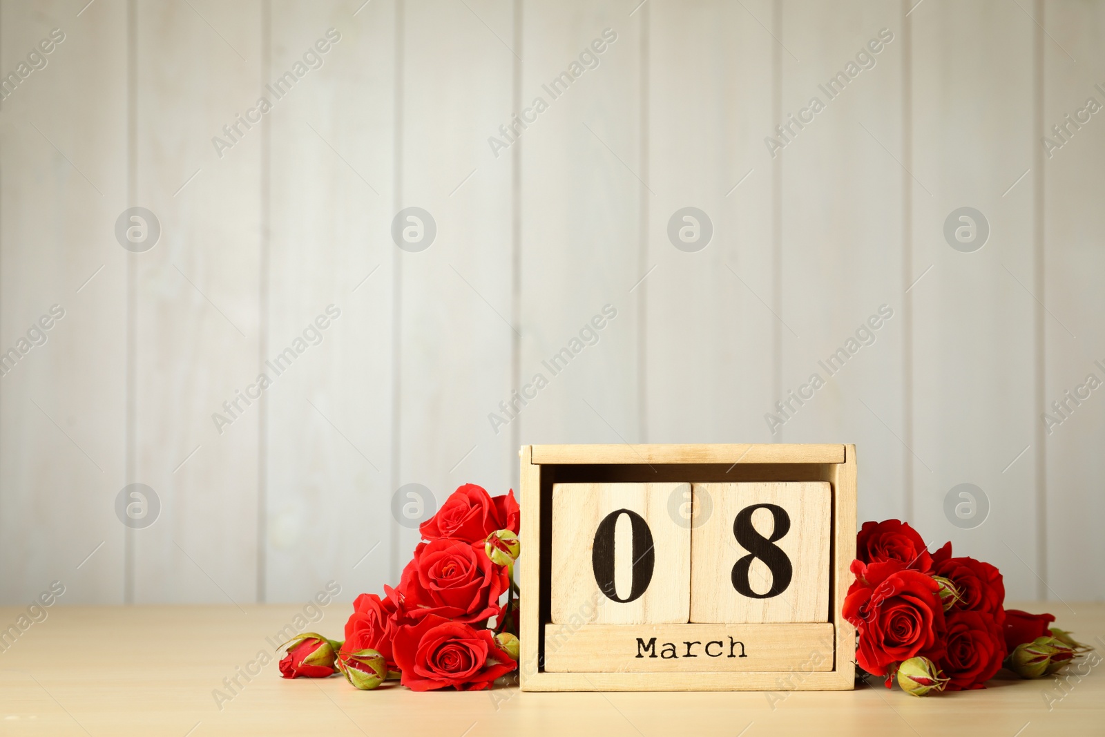 Photo of Wooden block calendar with date 8th of March and roses on table against light background, space for text. International Women's Day