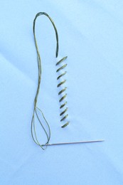 Photo of Sewing needle with thread and stitches on light blue cloth, top view