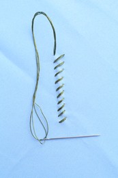 Sewing needle with thread and stitches on light blue cloth, top view