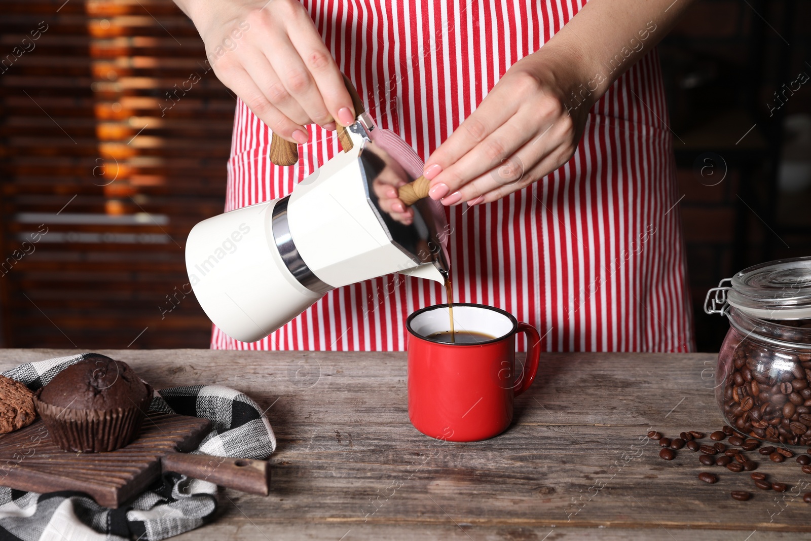 Photo of Woman pouring aromatic coffee from moka pot into cup at wooden table indoors, closeup