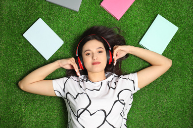 Photo of Young woman listening to audiobook while lying on grass, flat lay