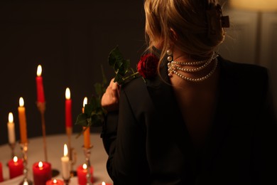 Photo of Woman wearing elegant jewelry near table with burning candles at night, back view