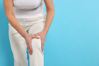 Arthritis symptoms. Woman suffering from pain in knee on light blue background, closeup. Space for text