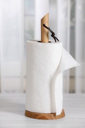 Photo of Holder with roll of paper towels on white wooden table indoors
