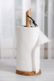 Holder with roll of paper towels on white wooden table indoors