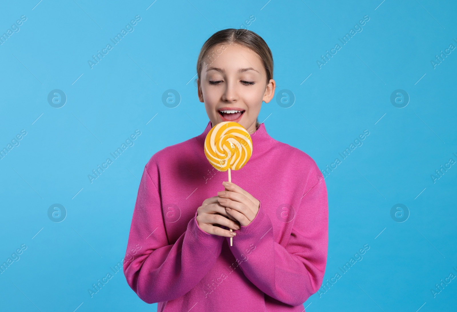 Photo of Teenage girl eating delicious lollipop on light blue background