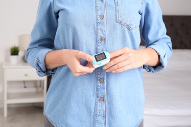 Photo of Young woman checking pulse with blood pressure monitor on finger, closeup