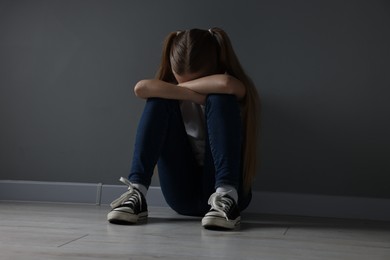 Photo of Sad girl sitting on floor near dark grey wall indoors