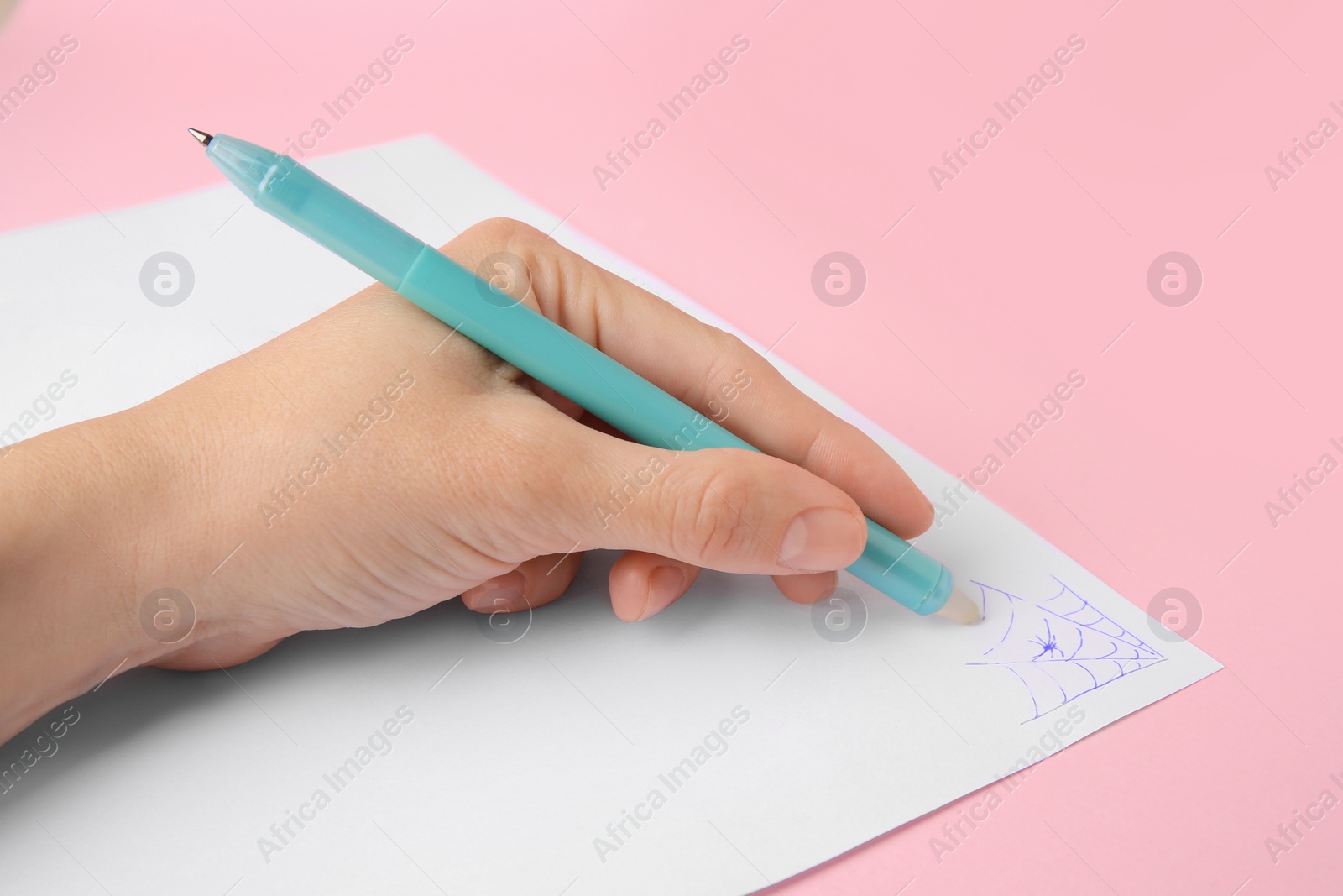 Photo of Woman erasing web drawn with erasable pen on sheet of paper against pink background, closeup