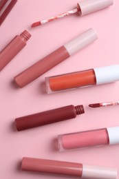 Photo of Different lip glosses and applicators on pink background, flat lay