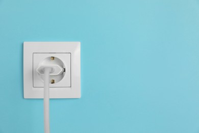 Photo of Charger adapter plugged into power socket on light blue wall, space for text. Electrical supply