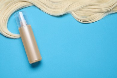 Photo of Spray bottle with thermal protection and lockblonde hair on light blue background, flat lay. Space for text