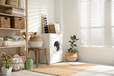 Photo of Modern washing machine and plants in laundry room interior