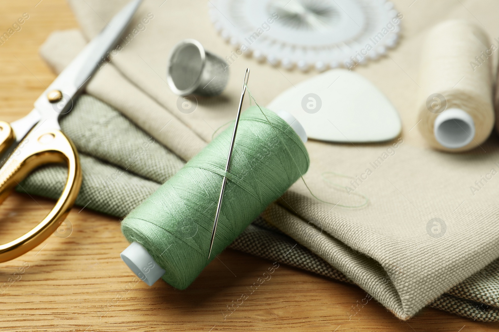 Photo of Spool of thread and sewing tools on wooden table, closeup